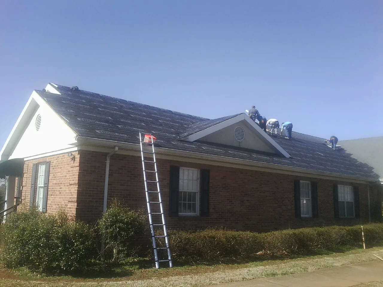 Crew tearing shingles off a brick ranch roof with a ladder set — Metal Roof Repair work by our crew in Apulia Station