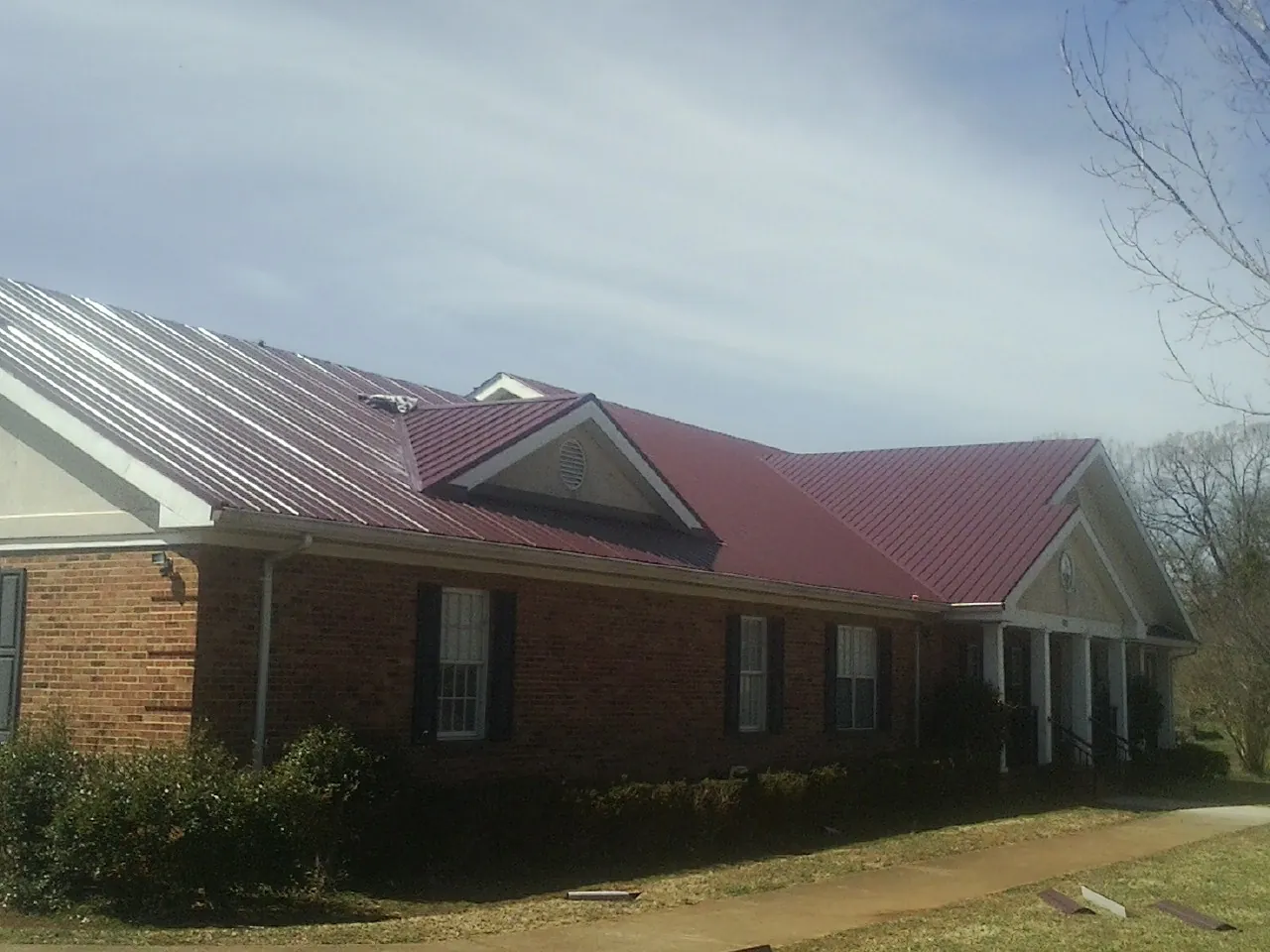 Red metal roof with gabled entries on a long brick building, from a Hail Damage Roof Repair job in Apulia Station