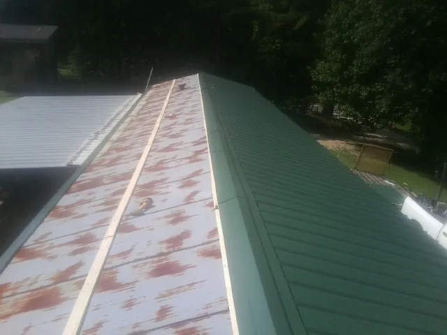 Old rusted panels beside newly installed green metal roofing — Wind Damage Roof Repair by Roofing Brothers in Apulia Station