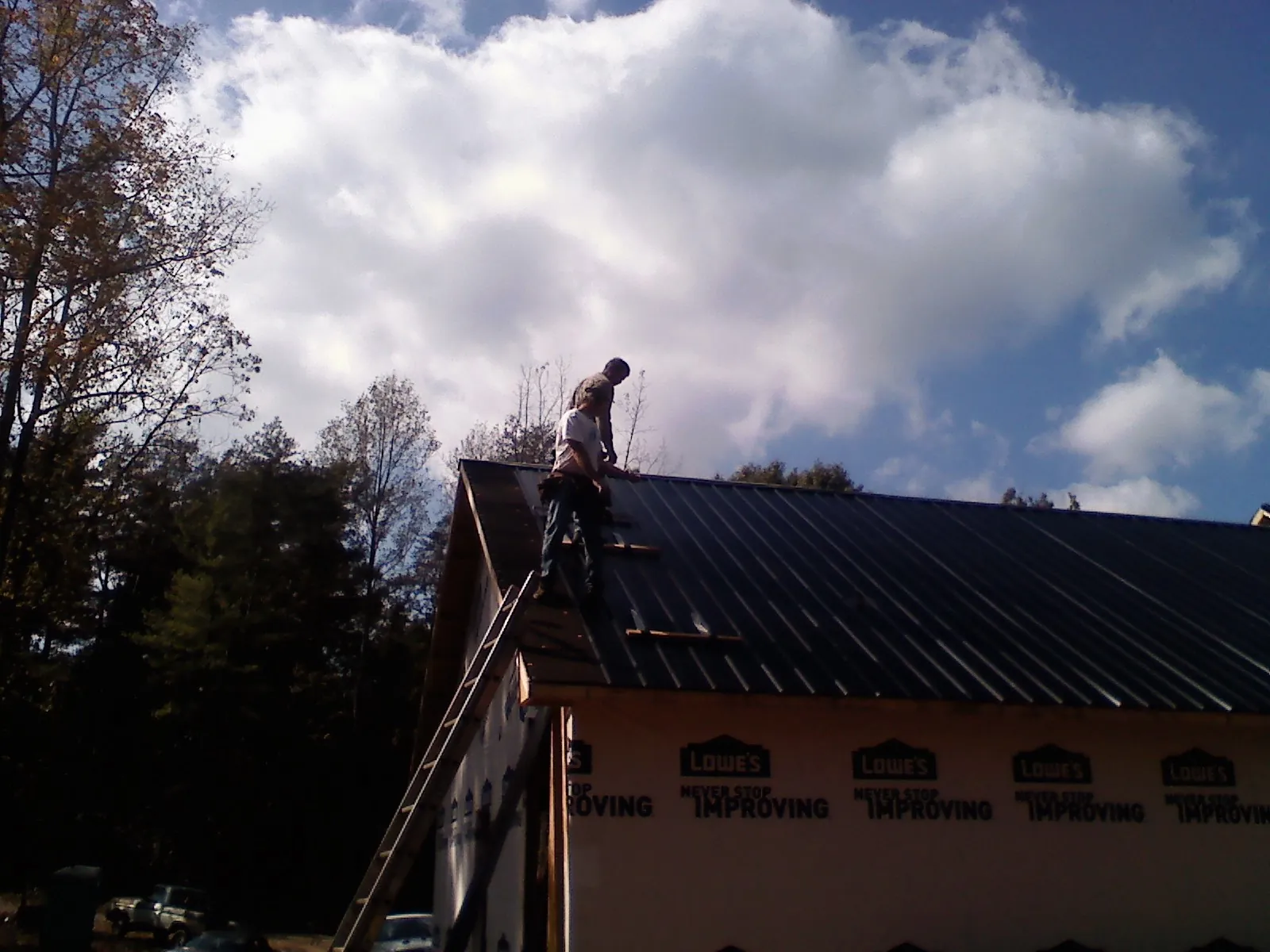 Roofer fastening dark metal panels high against a cloudy sky, from a Roof Inspection job in Apulia Station