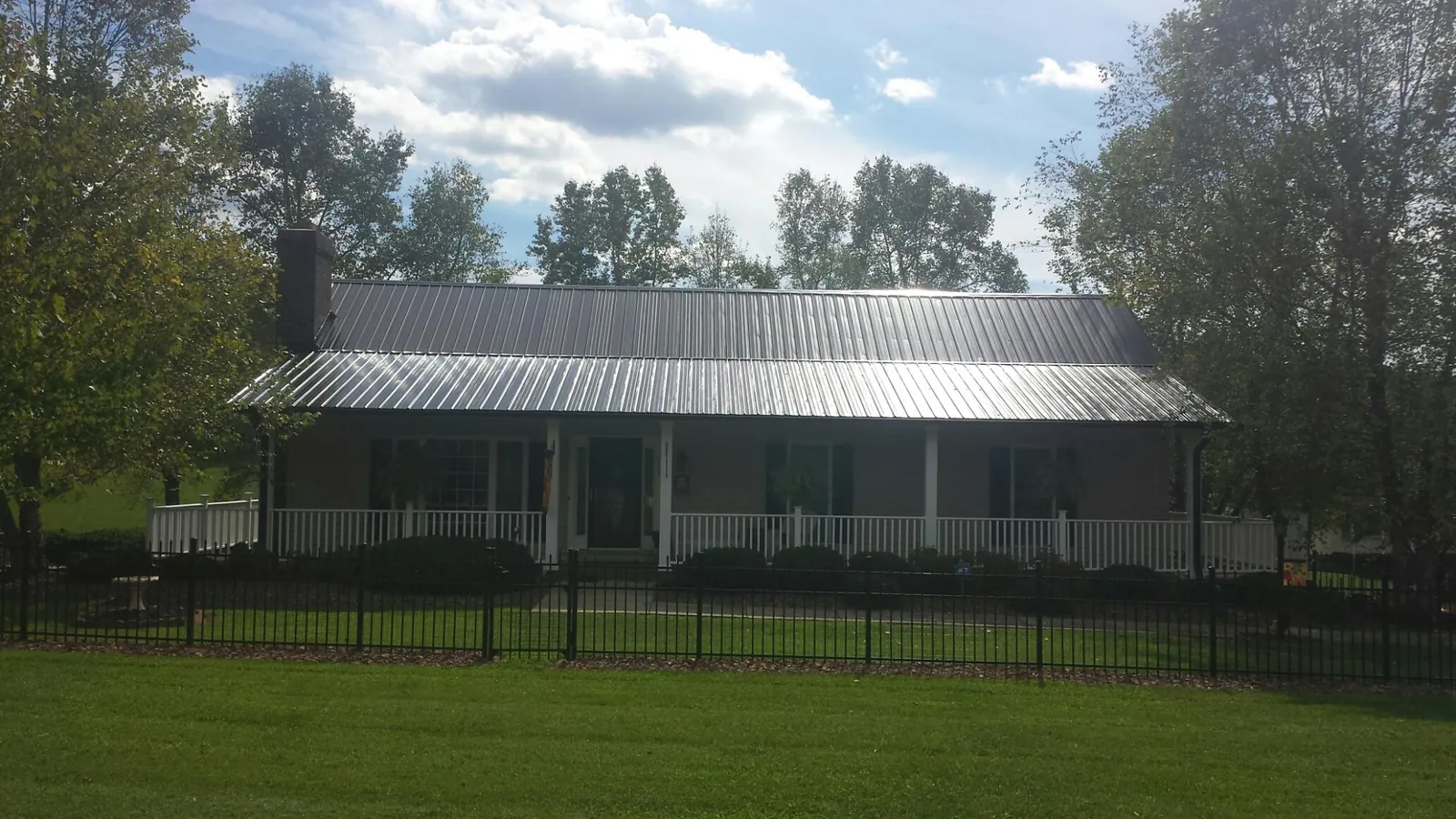 Gray metal roof on a brick ranch with a full width front porch — Gutter Guard Installation work by our crew in Apulia Station