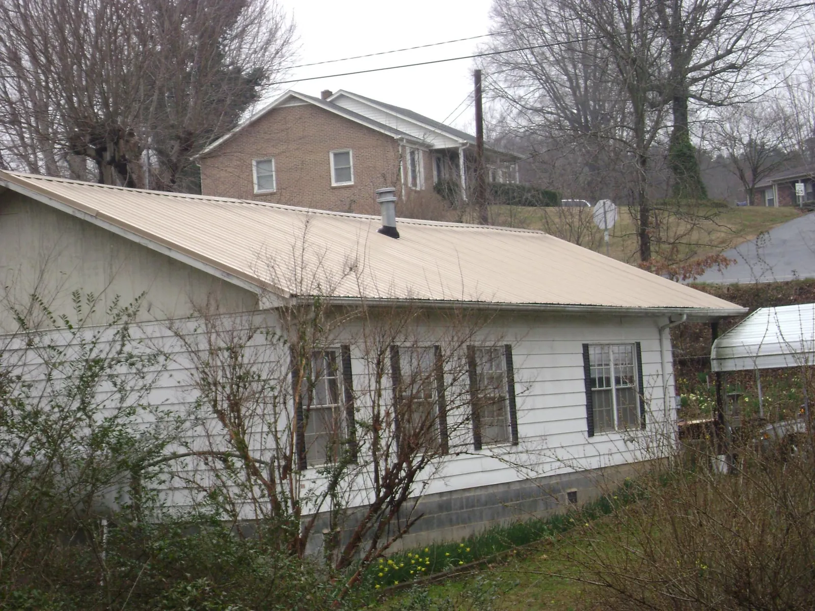 Tan metal roof on a white sided house set into a hillside — Commercial Roofing by Roofing Brothers in Apulia Station
