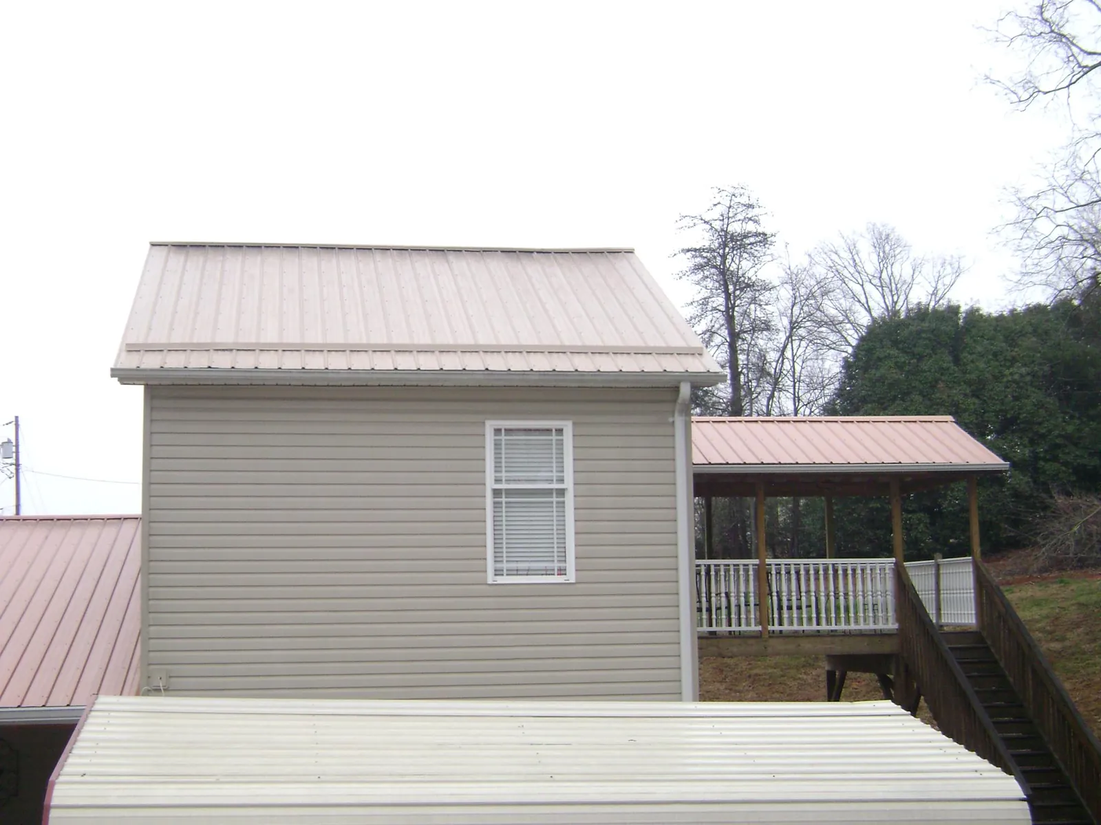 Tan metal roofs on a two story addition and attached porch, from a Roof Replacement job in Apulia Station
