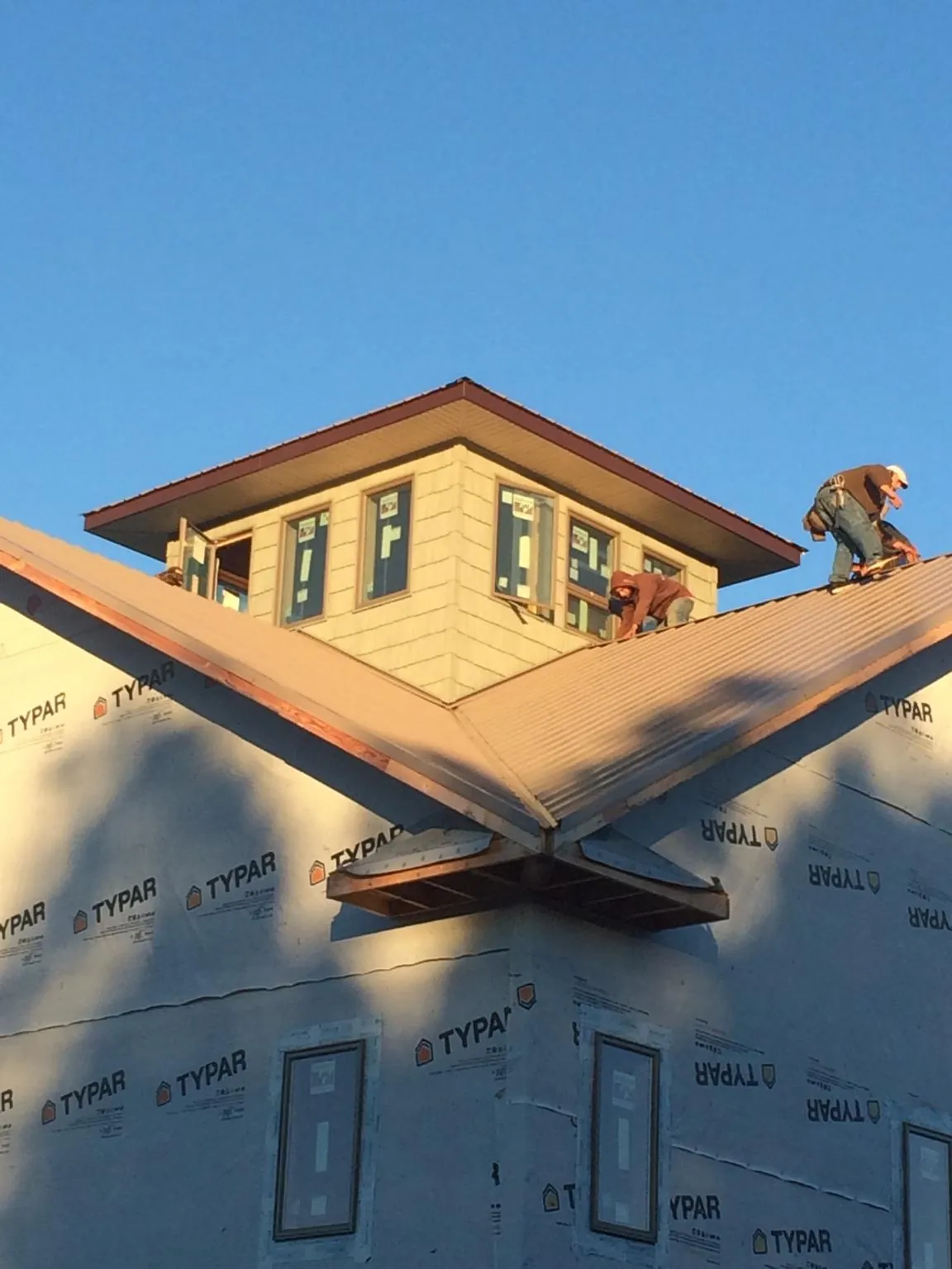 Roofers working around a rooftop cupola on a new metal roof at sunset in Apulia Station